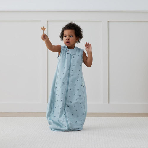 Child in a light blue sleeveless sleep sack with a star wand, standing on a white surface.