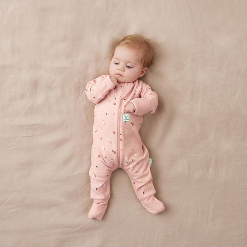 Baby in a pink onesie lying on a beige blanket