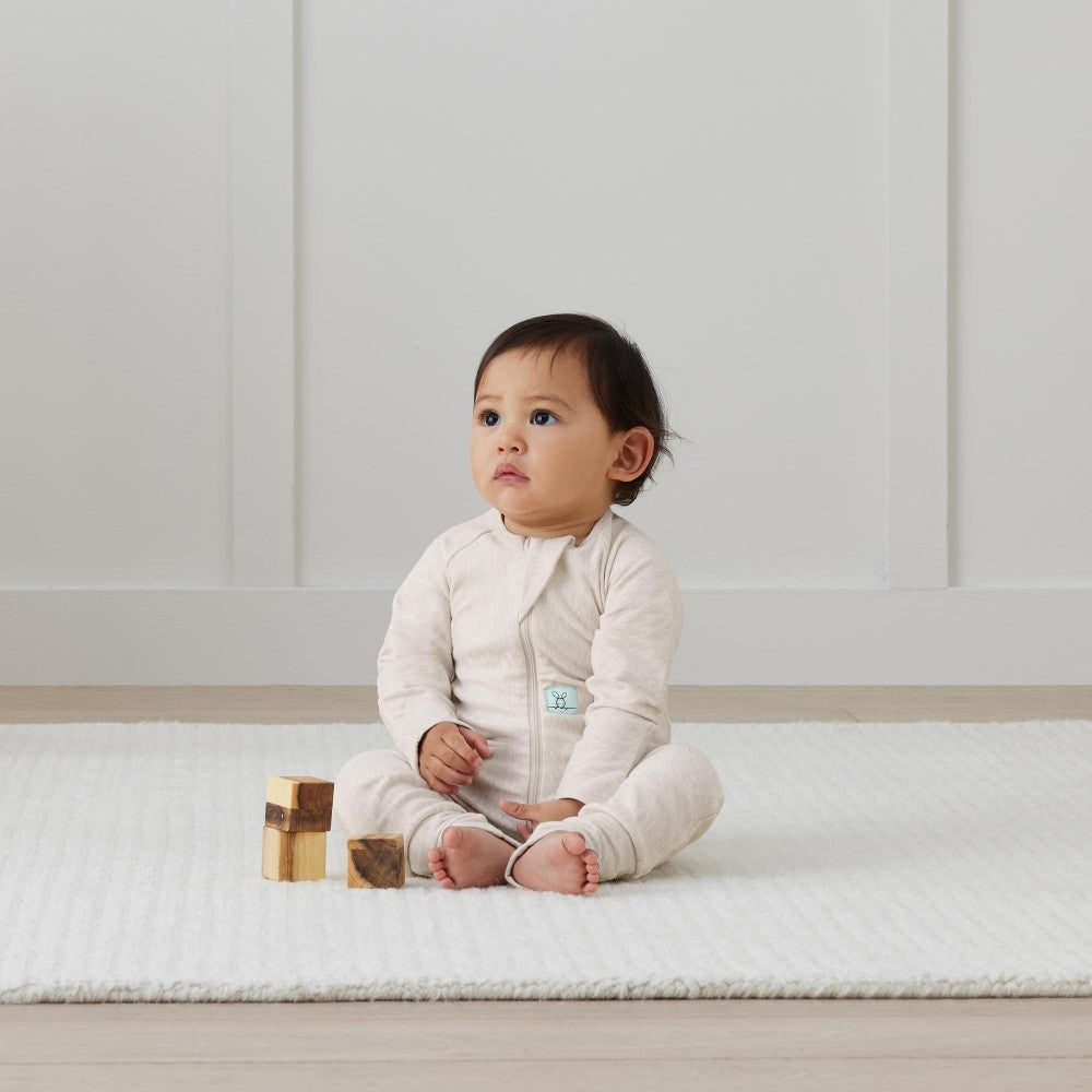 Baby sitting on a white mat with wooden blocks in a minimalistic room.