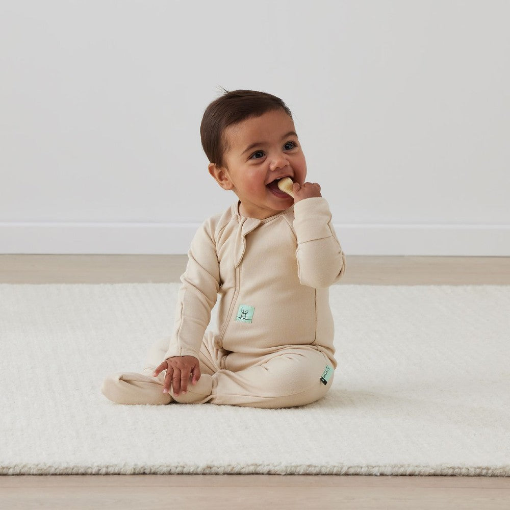 Baby in a beige onesie sitting on a white surface with a plain background