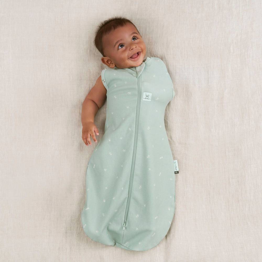 Baby wearing a light green sleep bag with white polka dots on a beige blanket.