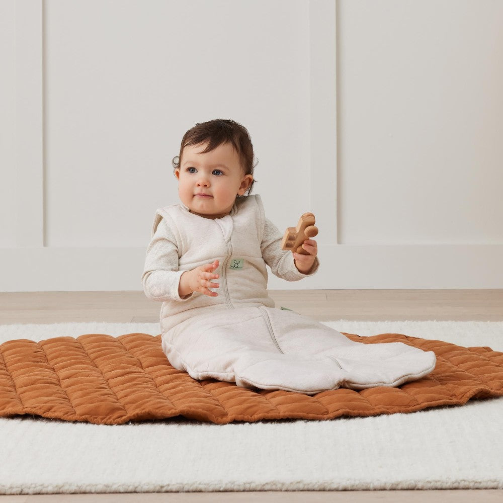 Baby sitting on a brown textured blanket in a minimalistic room.