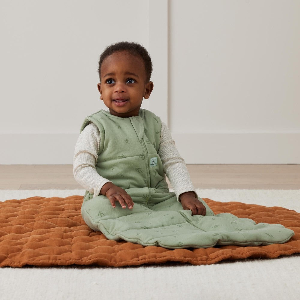 Child wearing a green baby sleeping bag on an orange blanket