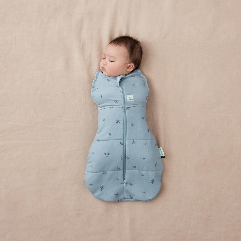 Baby sleeping in a blue sleep bag on a beige blanket
