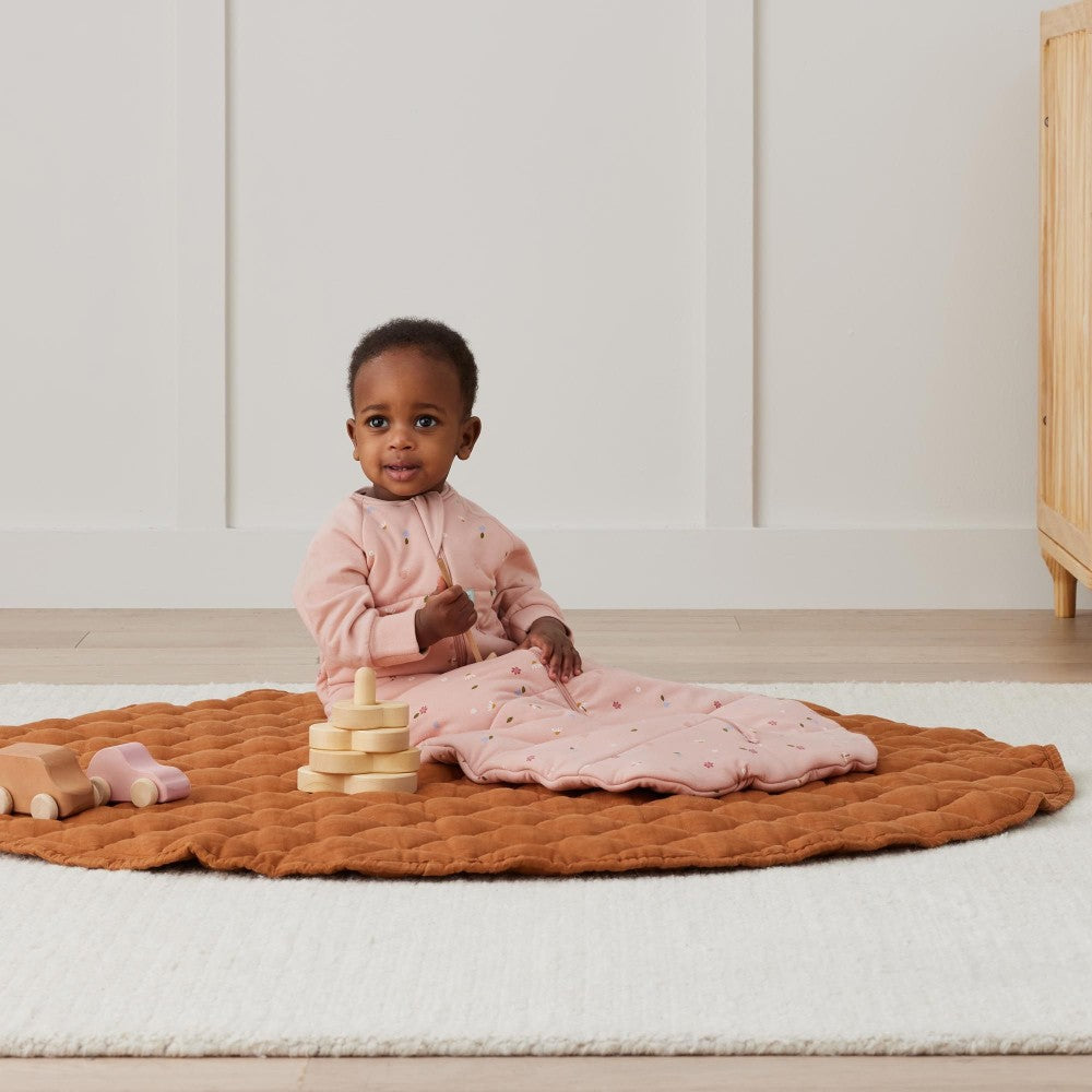 Child sitting on a brown mat with toys in a room.