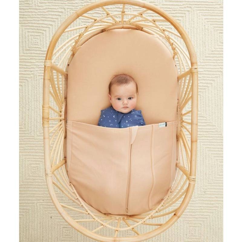 Baby in a woven bassinet with wheat hugme sheet on a textured beige background