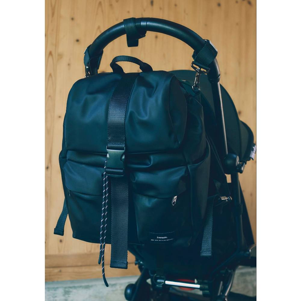 Black Finnson recycled polyester nappy backpack attached to a stroller against a wooden background