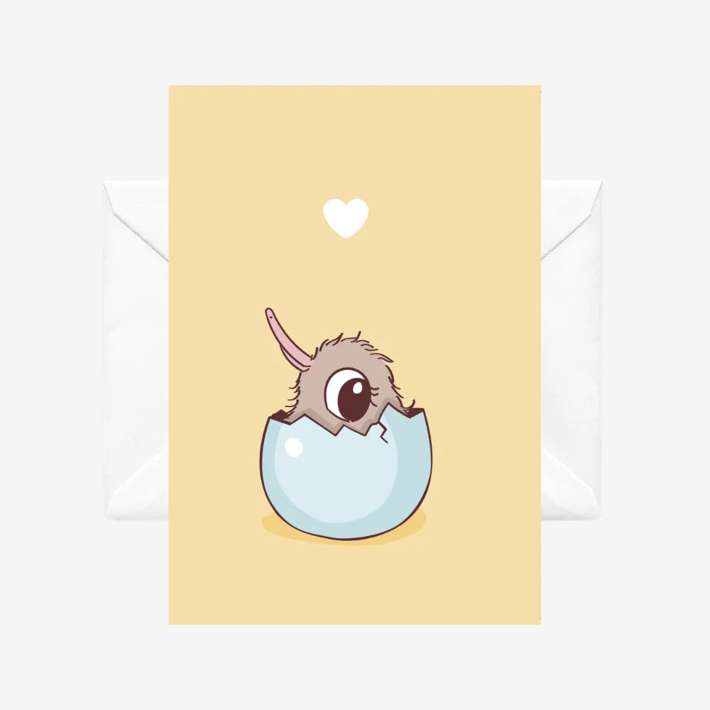 A yellow greeting card with a cartoon baby kiwi hatching out of an egg. There a white envelope behind it on a white background. 