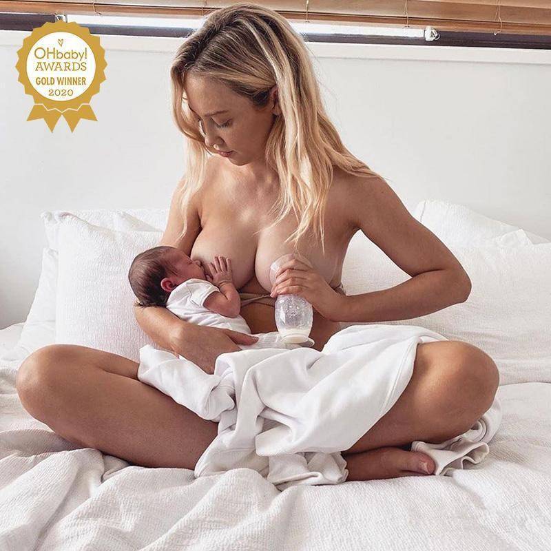 Mother breastfeeding with one silicone breastpump to aid let down on a bed 