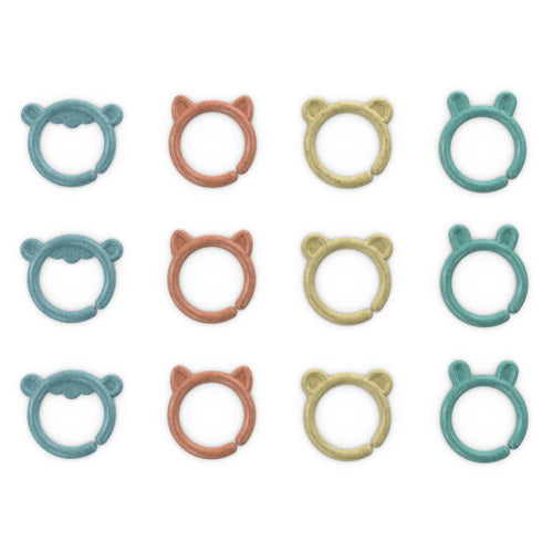 Twelve small ring-shaped baby teething toys arranged in a 3-by-4 grid on a white background. Each ring has a different animal face or ear design and comes in teal, peach, and pale yellow colors.