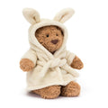 Brown Jellycat soft toy bear with cream robe against white background.