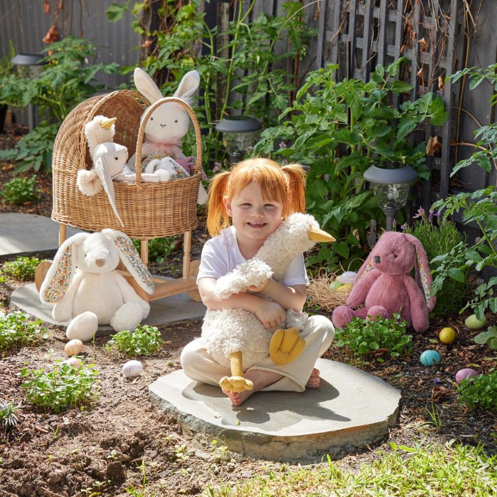 Child holding a stuffed animal in a garden with various plush toys and plants.