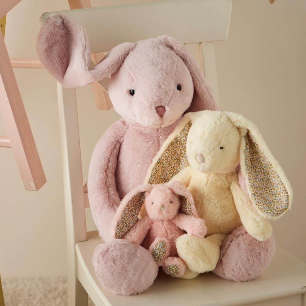 Three plush bunny toys in pink, yellow, and smaller pink toy on a chair.
