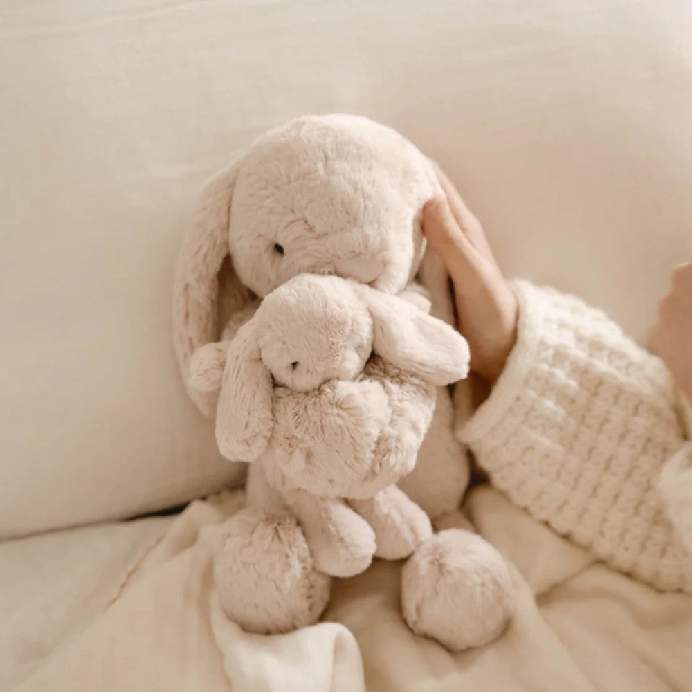 Jamie kay beige bunny soft toy sitting against pillow.