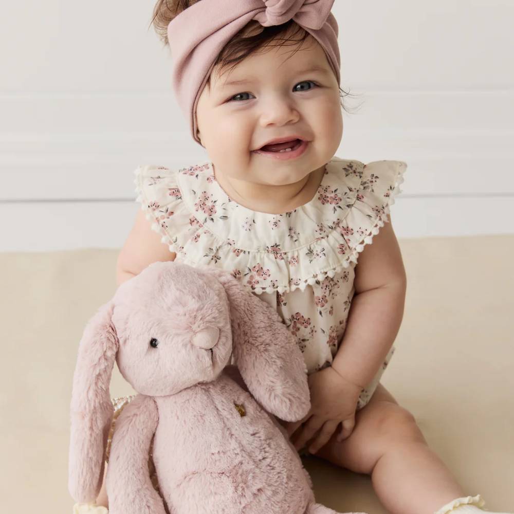Baby sitting with pink Jamie Kay bunny soft toy on floor.