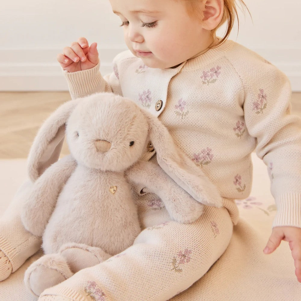 Baby sitting on floor with Beige Jamie Kay bunny soft toy.