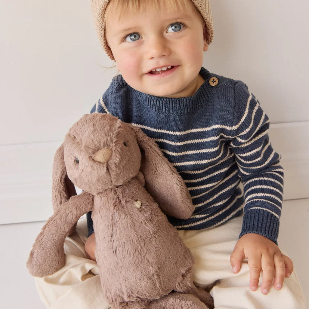 Baby sitting with Jamie Kay brown bunny soft toy on floor.
