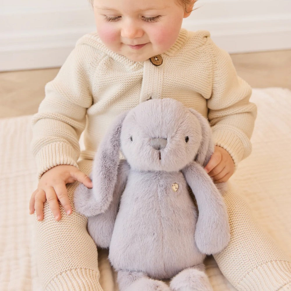 Baby sitting on floor with Grey Jamie Kay soft toy bunny.