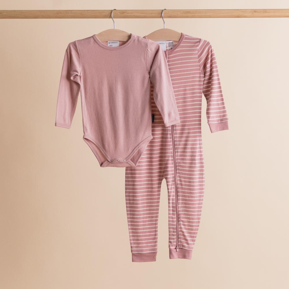Pink merino baby onesie and striped pants on hangers against a beige background