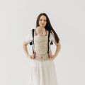 A woman wearing a golden colour baby carrier with a baby inside 