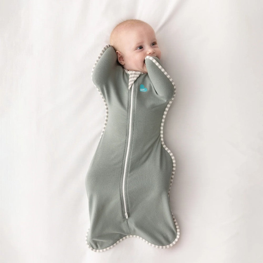 Baby wrapped in a olive green swaddle with a visible brand logo on a white background