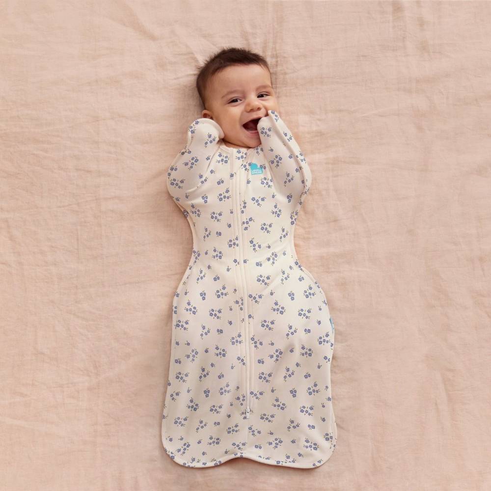 Baby lying on a pink blanket wearing a floral sleep swaddle.