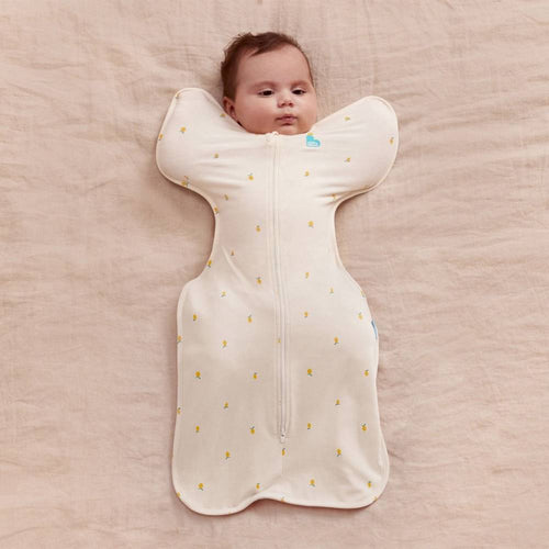Baby lying in a white sleep swaddle with yellow patterns on a beige surface