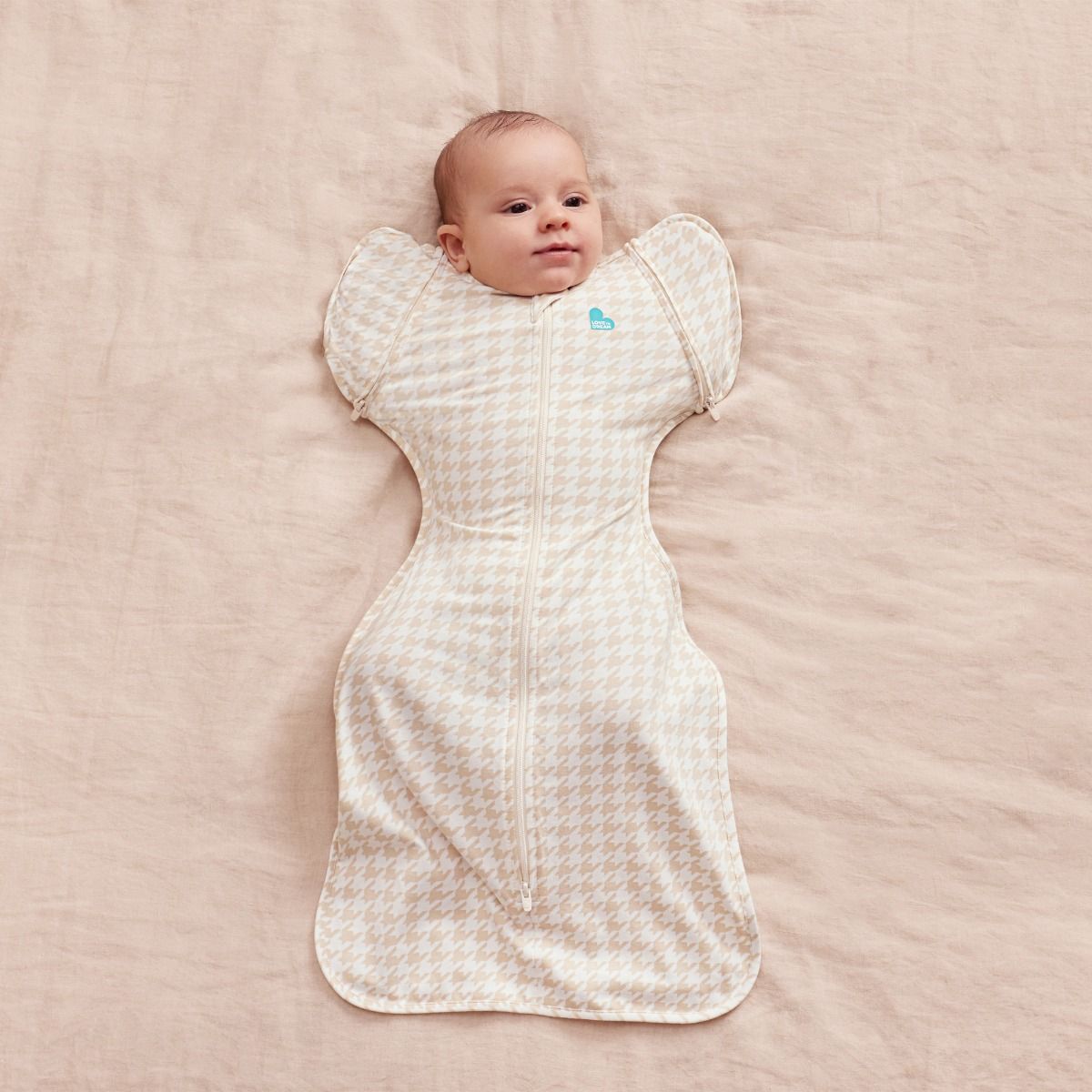 A baby lying down wearing a 1.0 tog Swaddle Up Transition Bag - Houndstooth Tan.