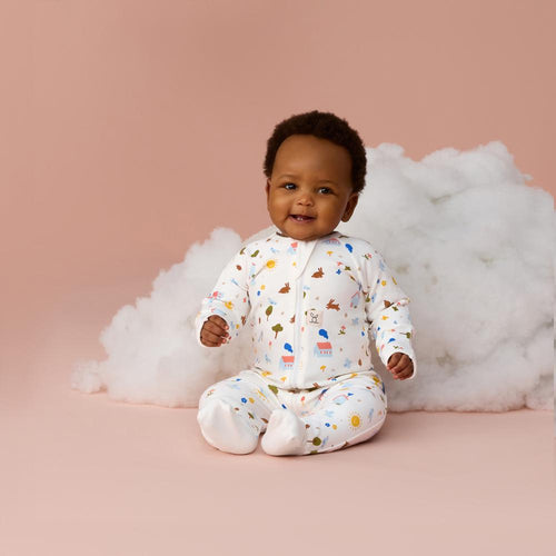 Baby in a patterned onesie sitting on a pink surface with white fluffy material