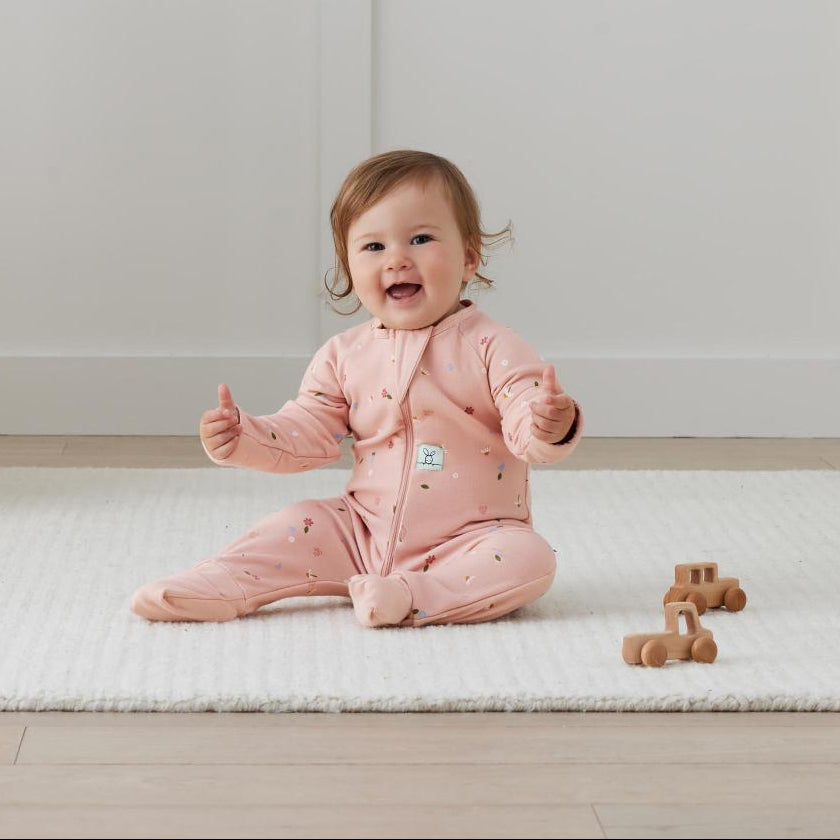 Baby in a pink outfit sitting on a white mat with wooden toys.