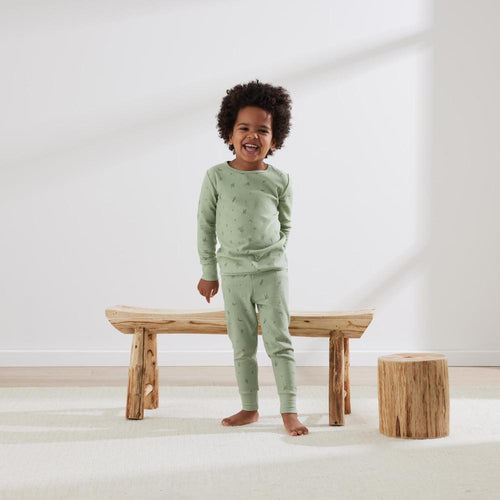 Child wearing green pajamas standing on a wooden bench in a minimalistic room.