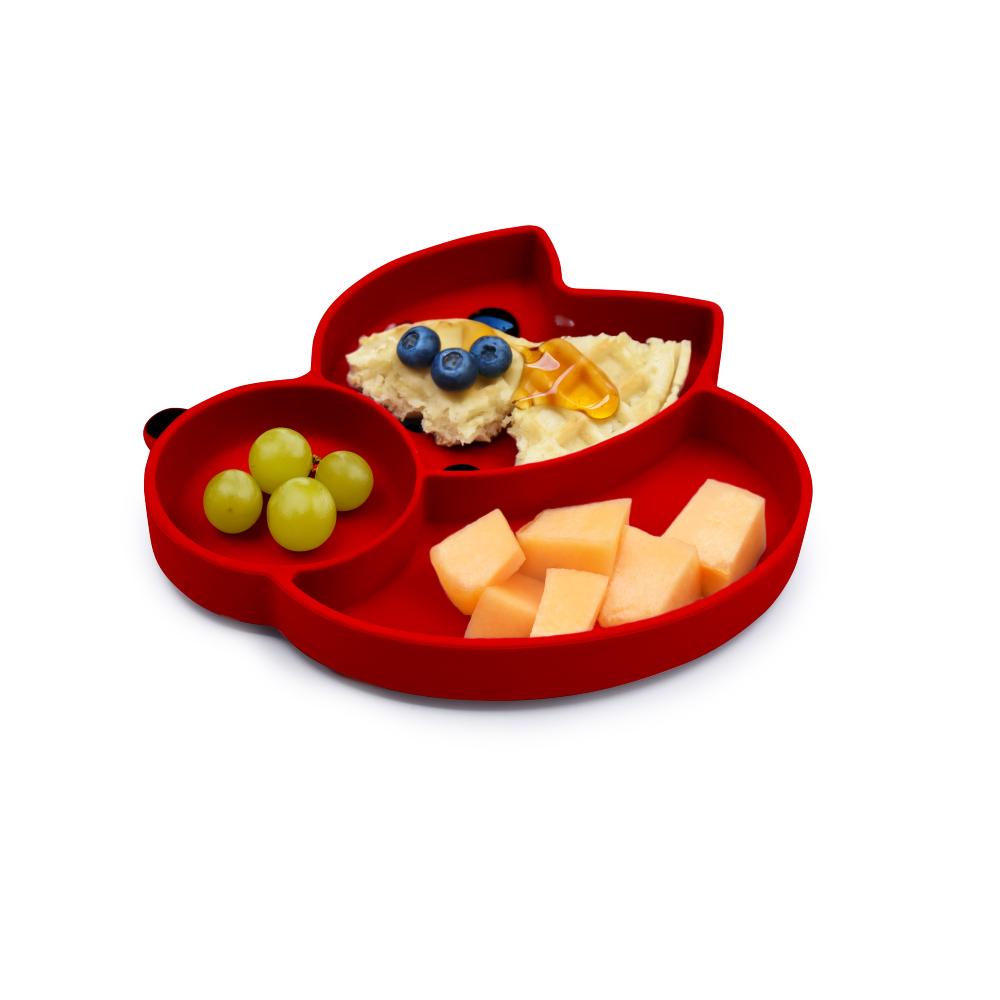 Red children's divided plate with compartments containing food on a white background