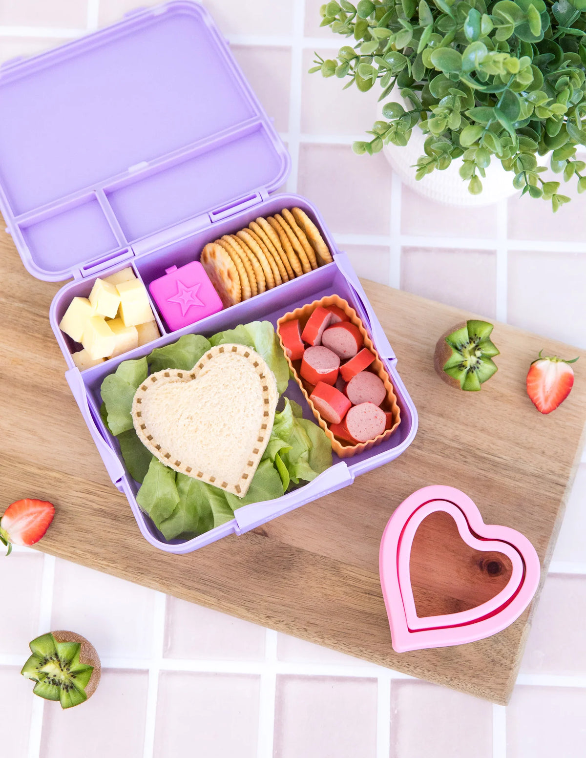 Full and colourful purple lunchbox with heart sandwich cutter to the side.  heart shaped sandwich is laid on top of the food in the lunchbox