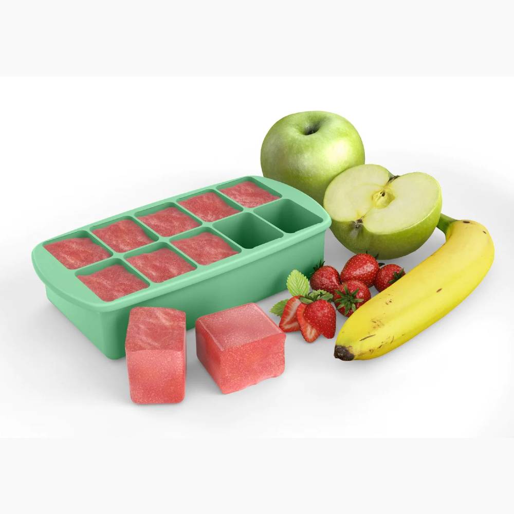 Green silicone baby food tray with fruit cubes next to a green apple, sliced banana, and strawberries on a white background