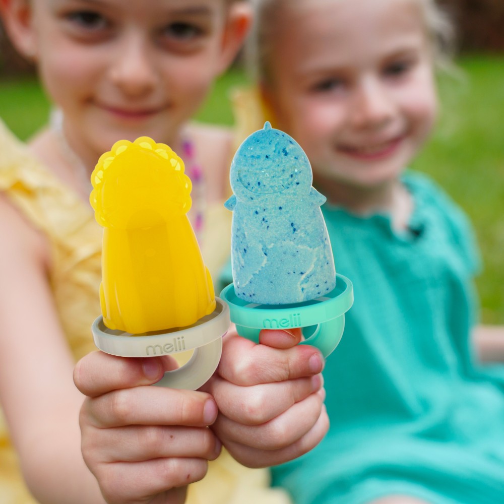 Two children holding yellow and blue popsicles with 'meli' holders outdoors.