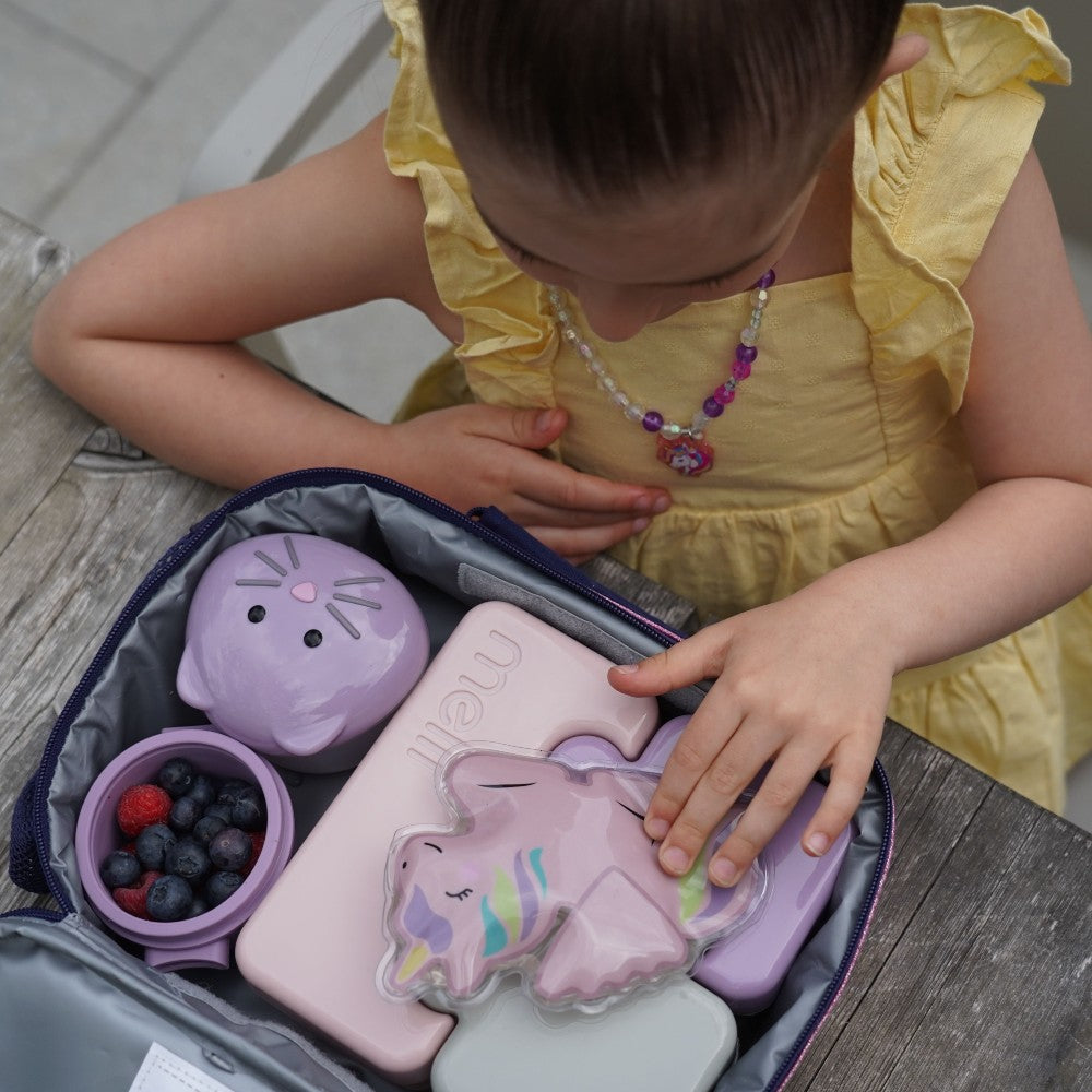 Child in a yellow dress interacting with purple unicorn-themed lunch boxes.