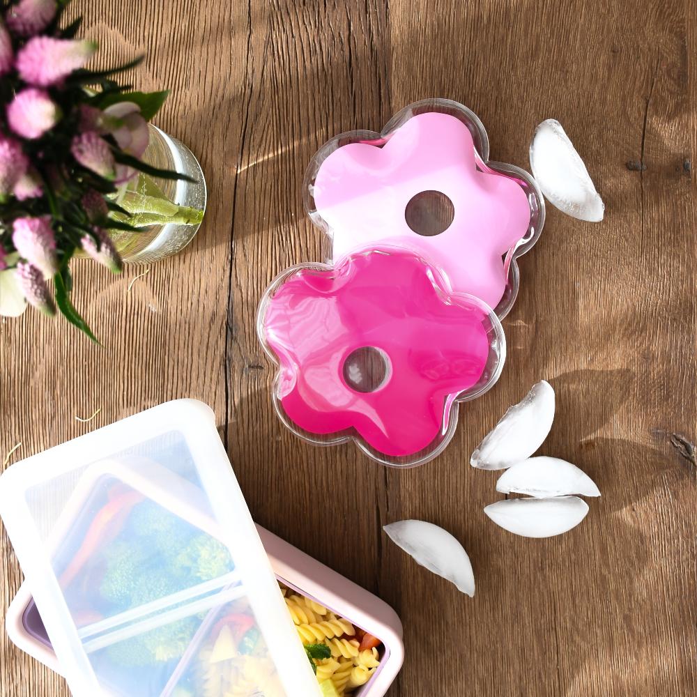 Pink flower-shaped ice cube tray on a wooden surface with ice cubes and a container of snacks.