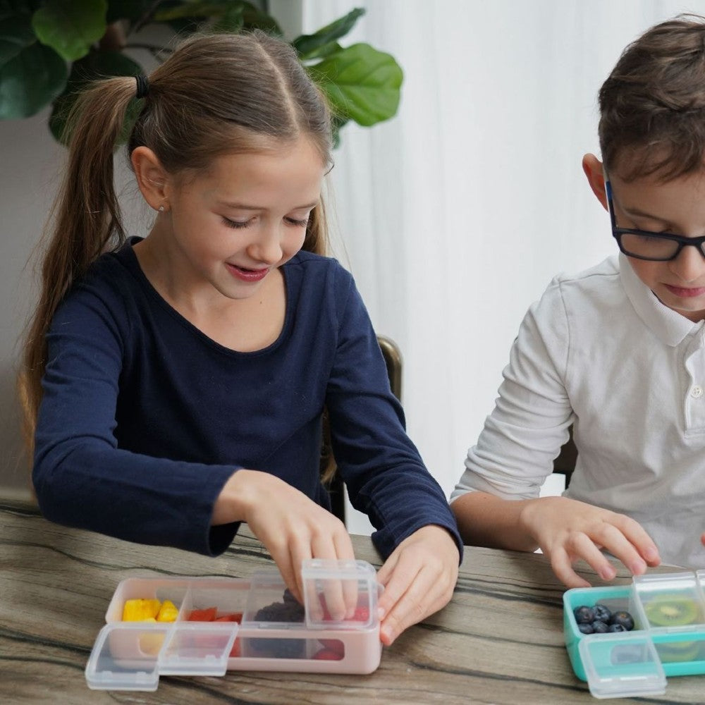 Two children sitting at a table with small containers filled with colorful snacks.