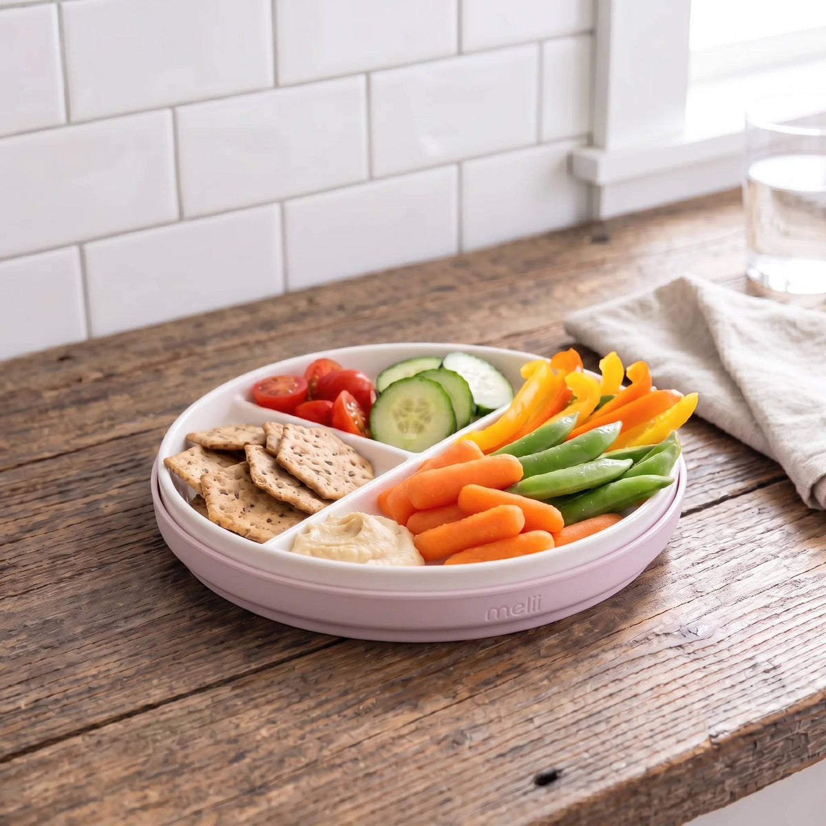 A divided ceramic plate with a pink silicone sleeve shown with a selection of food in each section. 