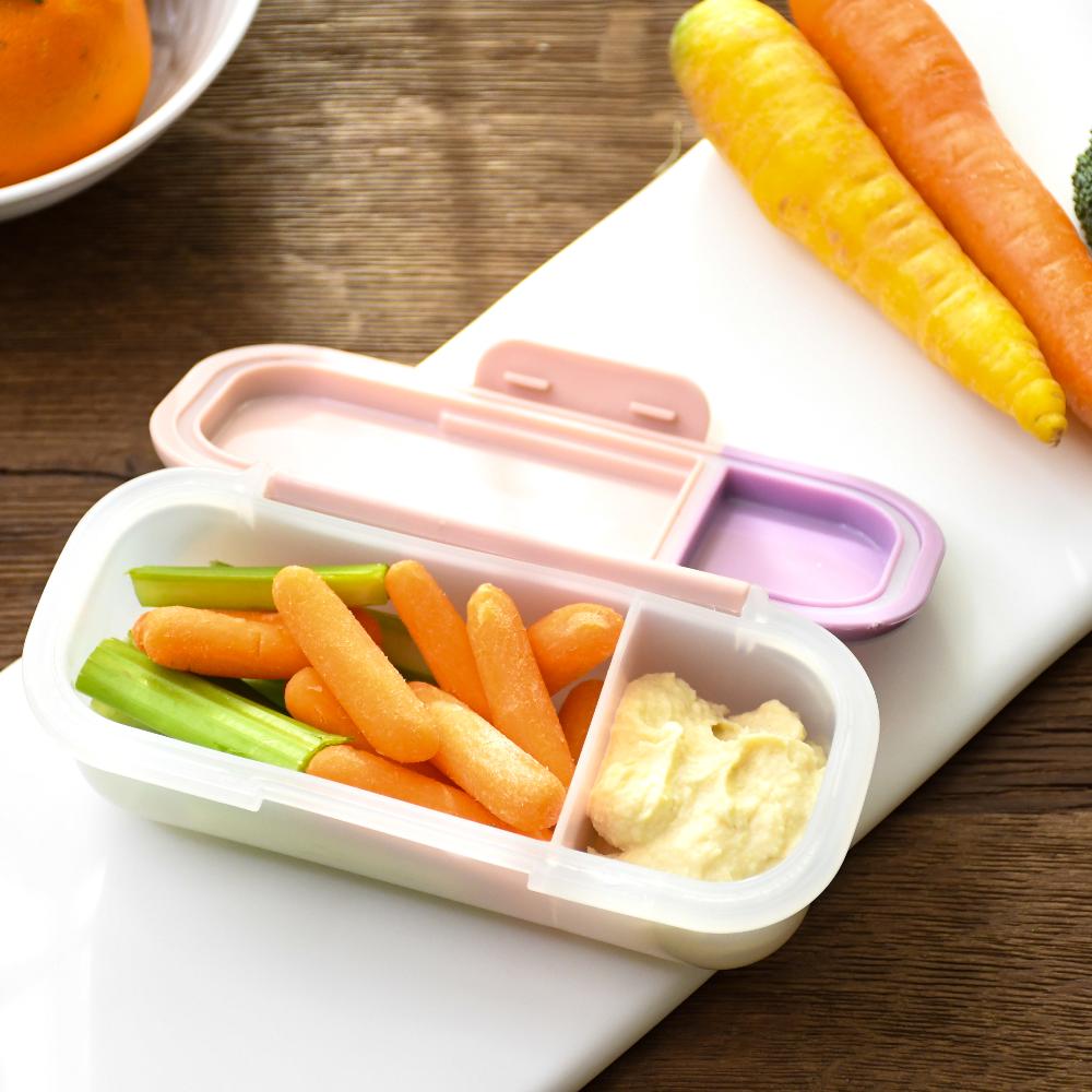 Children's lunchbox with compartments containing carrots, celery, and cauliflower on a wooden surface.