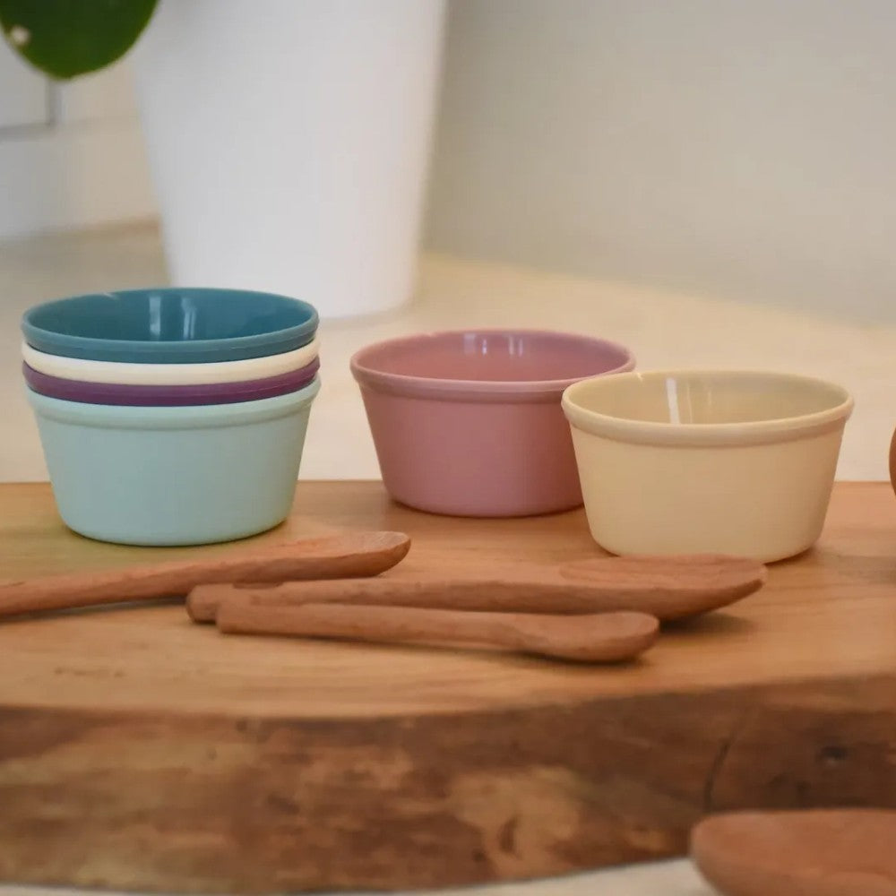 Set of colorful silicone baking and food display cups and wooden spoons on a wooden surface.
