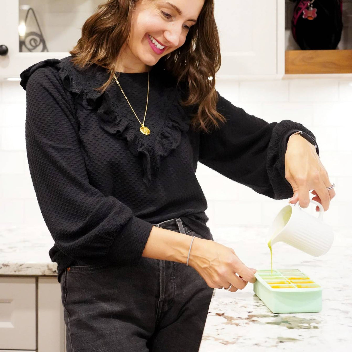 A woman pouring puree into a sage freezer tray. 