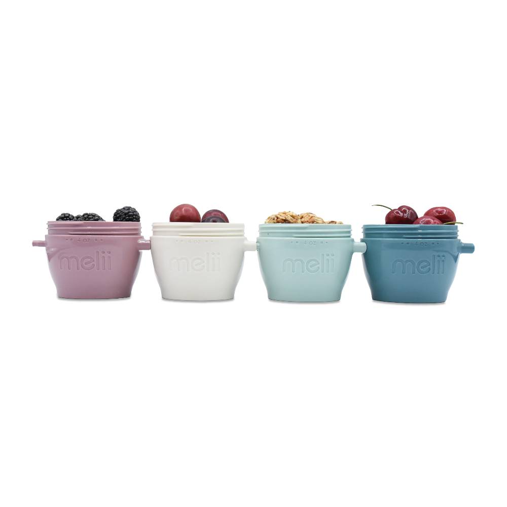 Four small containers with lids in pastel colors filled with fruits on a white background
