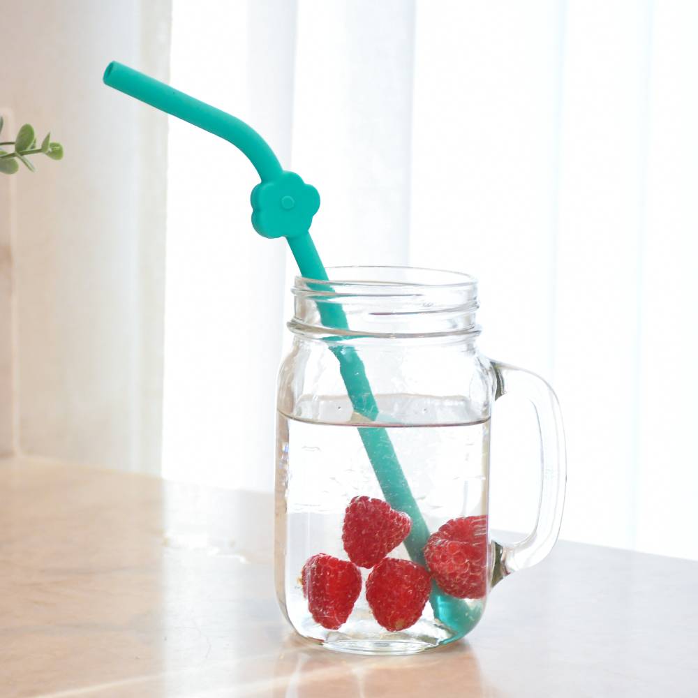 Glass mug with strawberries and a teal straw on a light background