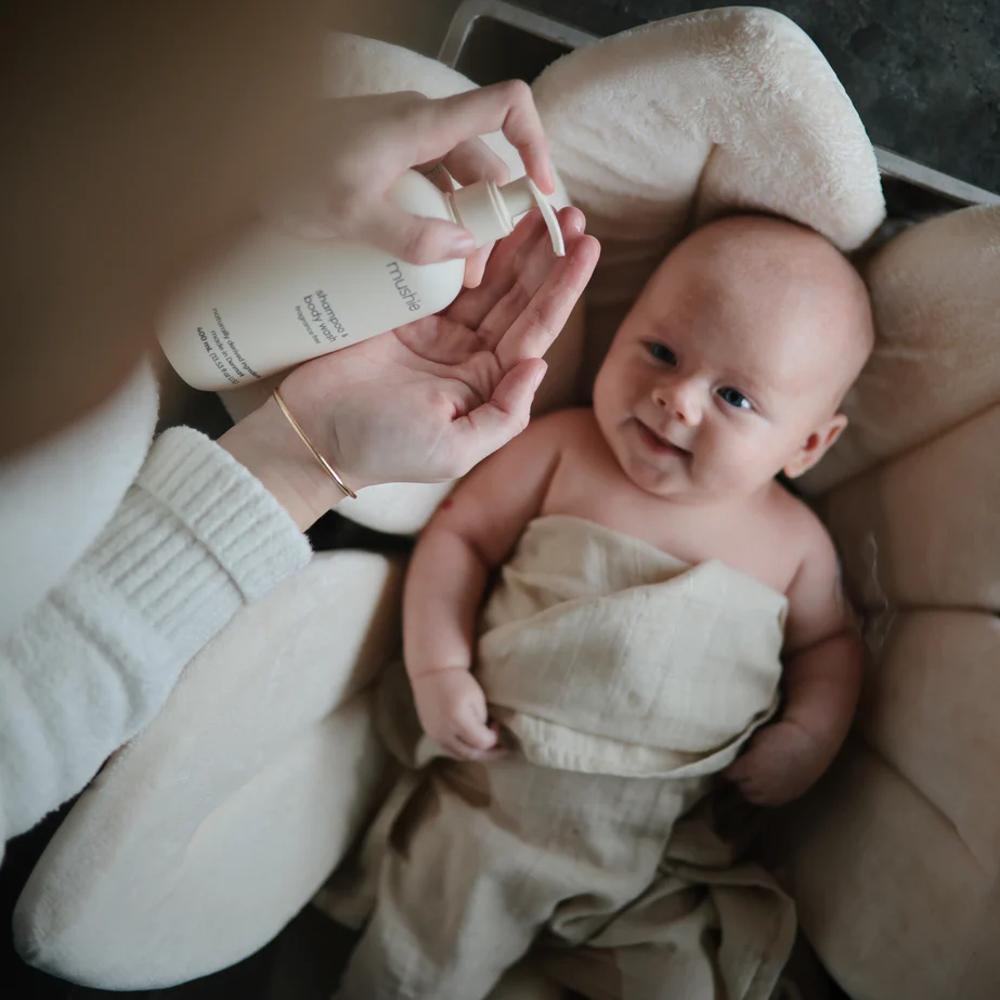 Baby wrapped in a towel being held by an adult with a bottle of lotion.