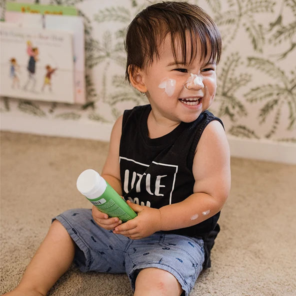 Child holding green tube of moisturiser with cream on his face in a bedroom setting