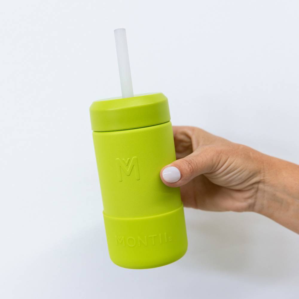 A hand holding a matcha green smoothie cup with silicone straw. 