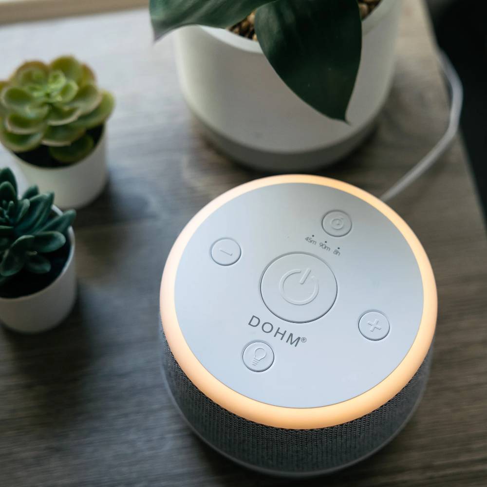 Yogasleep Dohm Nova white noise machine on a wooden surface with plants in the background