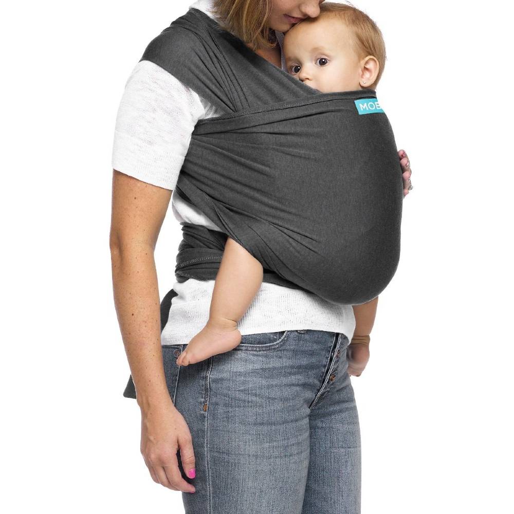 Mum carrying baby in grey Moby baby carrier against white background.
