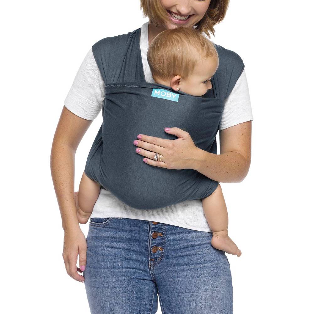 Mum carrying baby in blue Moby baby carrier against white background.